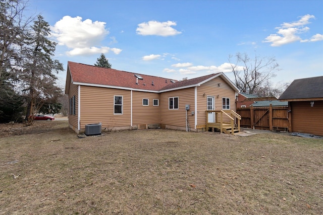 rear view of house with a lawn, roof with shingles, central AC, and fence