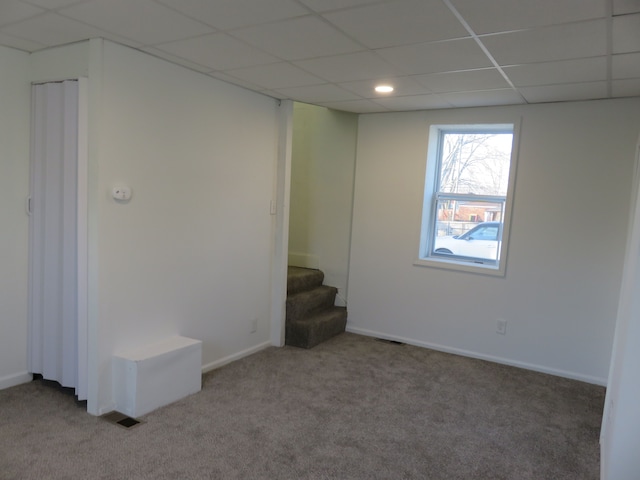 carpeted empty room featuring stairway, a paneled ceiling, and baseboards