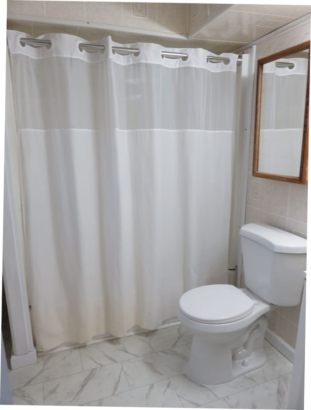 bathroom featuring a shower with curtain, toilet, and marble finish floor