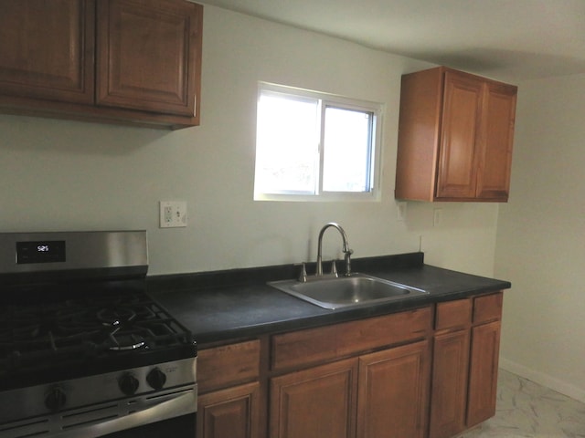 kitchen featuring a sink, marble finish floor, stainless steel gas range oven, dark countertops, and brown cabinets