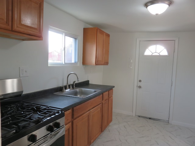 kitchen with stainless steel gas range oven, dark countertops, brown cabinetry, marble finish floor, and a sink