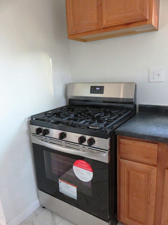 kitchen featuring dark countertops, baseboards, brown cabinets, marble finish floor, and gas stove