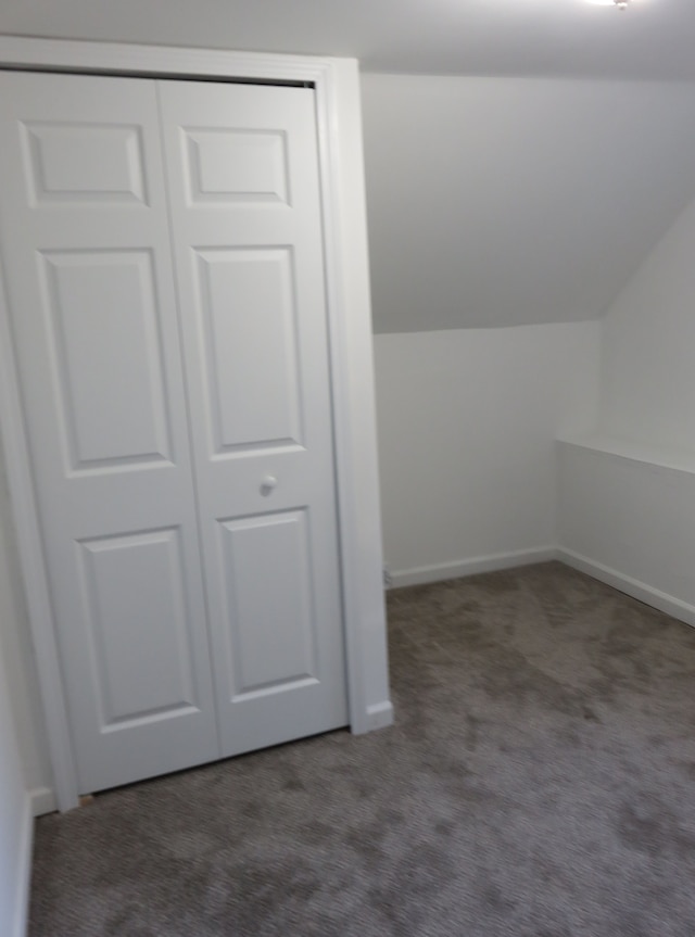 additional living space featuring baseboards, lofted ceiling, and dark colored carpet