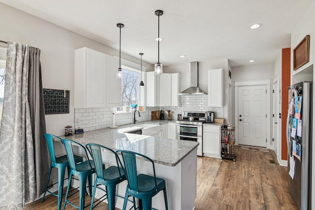 kitchen featuring white cabinets, appliances with stainless steel finishes, a peninsula, and wall chimney range hood