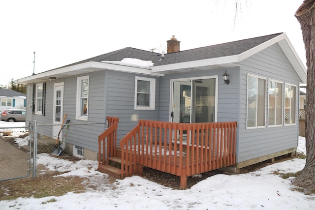 snow covered property with a chimney, fence, and a shingled roof