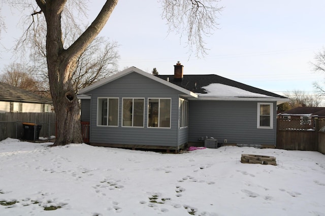 snow covered house with central air condition unit, a chimney, and fence