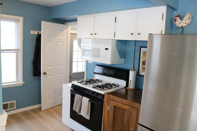 kitchen featuring visible vents, light wood-style flooring, freestanding refrigerator, gas stove, and white microwave