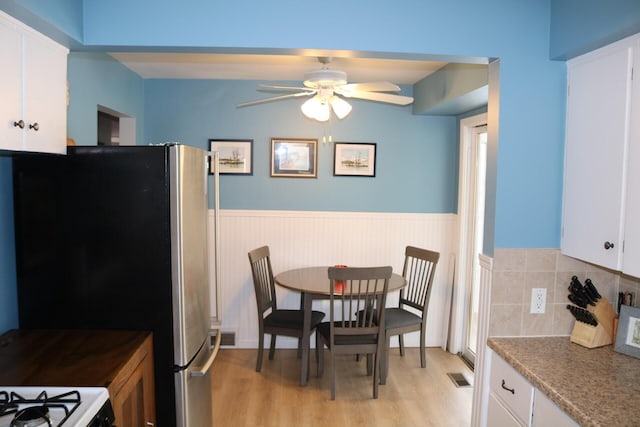 interior space with a wainscoted wall, white cabinets, light wood-style flooring, and visible vents