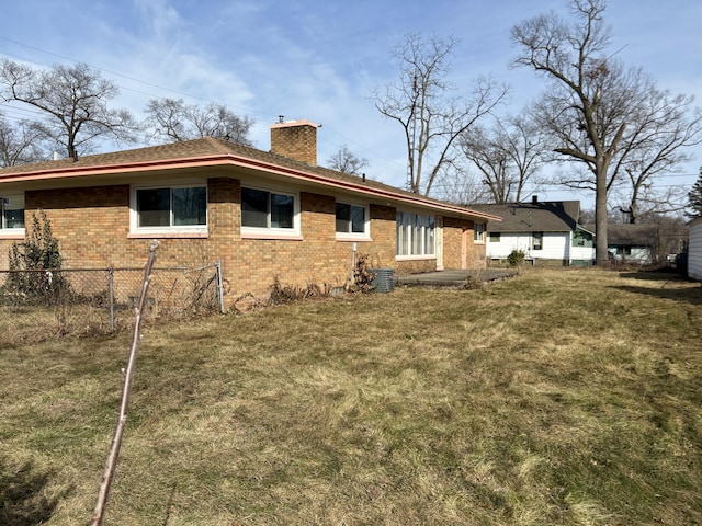 exterior space featuring brick siding, a chimney, a yard, and fence