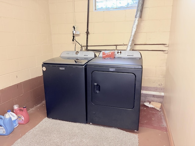 washroom with concrete block wall, independent washer and dryer, and laundry area