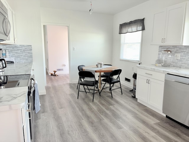 kitchen featuring light wood-type flooring, stainless steel appliances, light stone counters, and baseboards