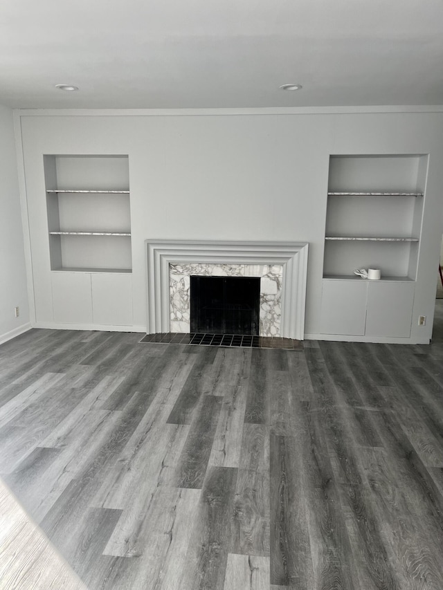 unfurnished living room with built in features, wood finished floors, a fireplace, and ornamental molding