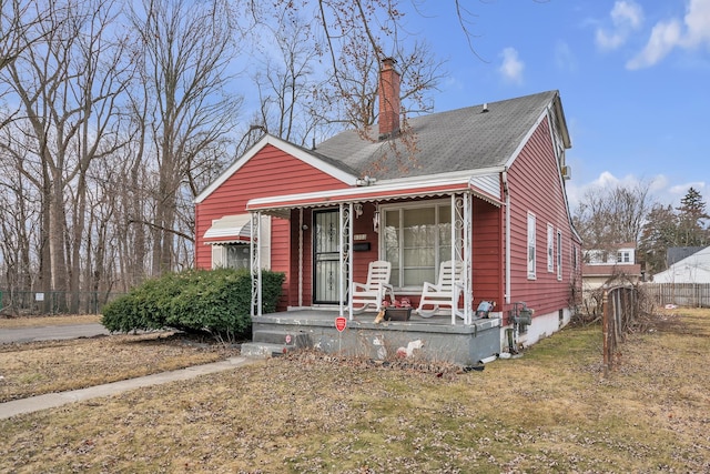 view of front facade with covered porch, a chimney, a front yard, and fence