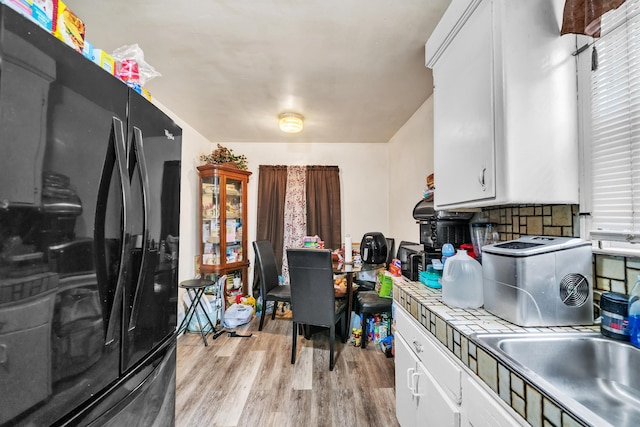 kitchen featuring light wood-type flooring, a sink, backsplash, white cabinetry, and freestanding refrigerator