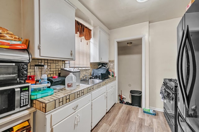 kitchen with a sink, light wood-style floors, black appliances, and white cabinetry