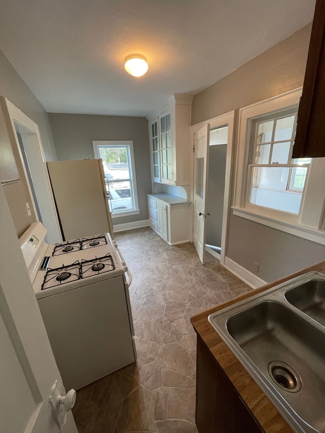 kitchen featuring glass insert cabinets, baseboards, white appliances, white cabinetry, and a sink