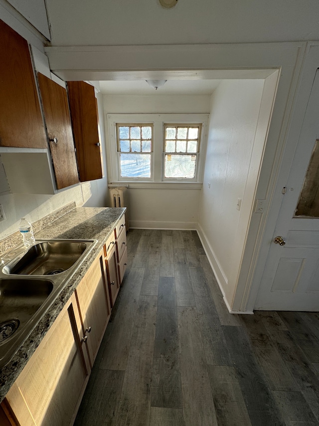 kitchen with dark wood-type flooring, baseboards, radiator heating unit, brown cabinetry, and a sink