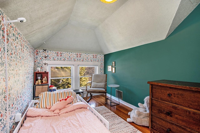 bedroom with visible vents, lofted ceiling, a textured ceiling, wood finished floors, and baseboards