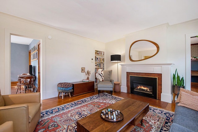 living area with a brick fireplace, built in shelves, wood finished floors, and ornamental molding