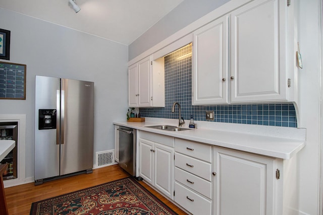 kitchen featuring backsplash, appliances with stainless steel finishes, light wood-style floors, white cabinets, and a sink