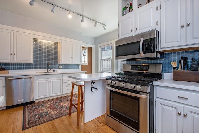 kitchen with a sink, stainless steel appliances, light wood-style floors, white cabinets, and light countertops