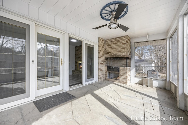 unfurnished sunroom with an outdoor brick fireplace and a ceiling fan