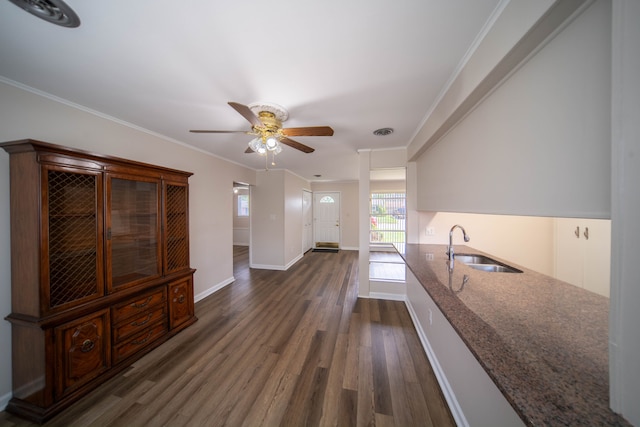 interior space featuring a ceiling fan, dark wood finished floors, dark stone counters, a sink, and crown molding