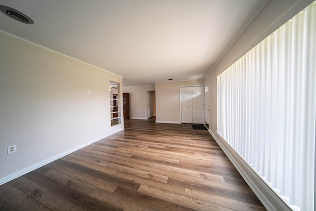 spare room with ornamental molding, wood finished floors, visible vents, and baseboards