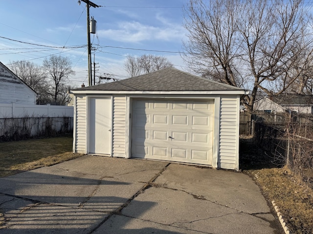 detached garage featuring concrete driveway and fence