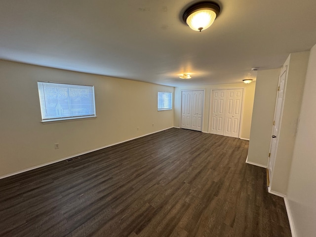 unfurnished bedroom with dark wood finished floors, visible vents, multiple closets, and baseboards