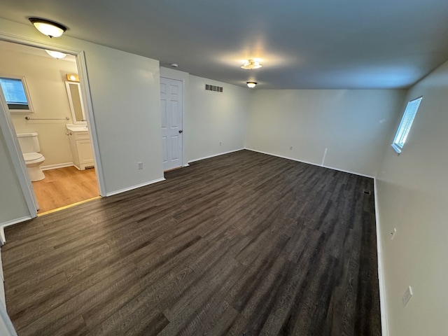 unfurnished bedroom featuring visible vents, baseboards, dark wood-type flooring, and ensuite bath