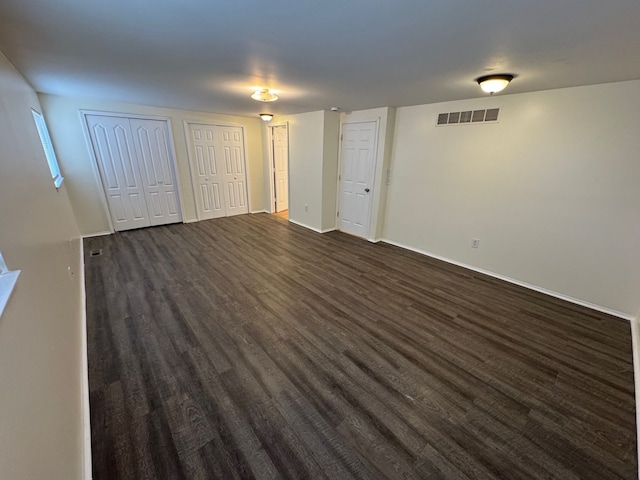 unfurnished bedroom featuring visible vents, two closets, dark wood-type flooring, and baseboards