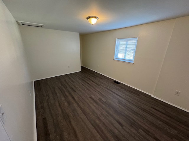 spare room with visible vents, baseboards, attic access, and dark wood-style flooring