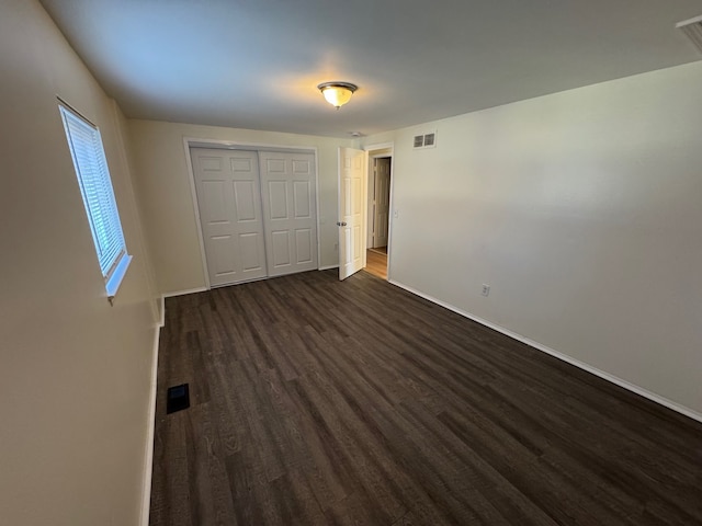 unfurnished bedroom with visible vents, baseboards, a closet, and dark wood finished floors