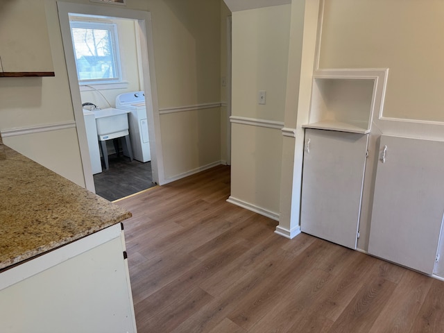 kitchen with light stone counters, washer / clothes dryer, light wood-type flooring, and baseboards