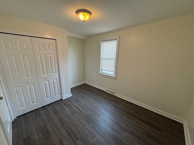 unfurnished bedroom featuring visible vents, baseboards, dark wood-type flooring, and a closet