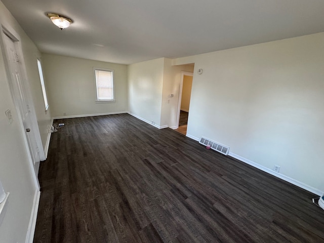 empty room featuring visible vents, baseboards, and dark wood-type flooring