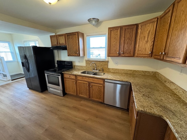 kitchen featuring brown cabinets, a sink, under cabinet range hood, appliances with stainless steel finishes, and light wood finished floors