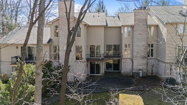 rear view of property featuring cooling unit, brick siding, roof with shingles, and a chimney