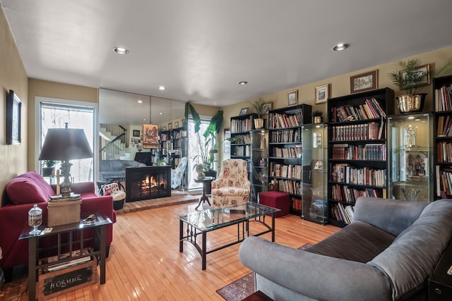 living room featuring wood-type flooring, plenty of natural light, and a warm lit fireplace