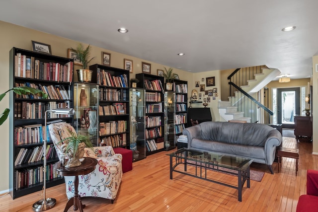 sitting room featuring wall of books, stairway, recessed lighting, and hardwood / wood-style floors