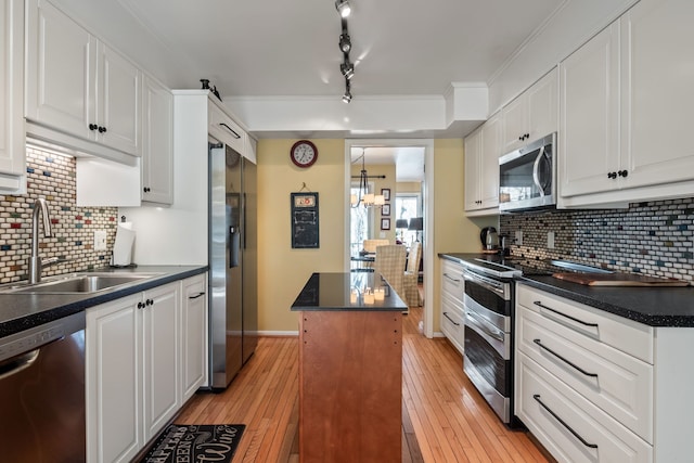 kitchen with dark countertops, light wood-type flooring, appliances with stainless steel finishes, white cabinets, and a sink