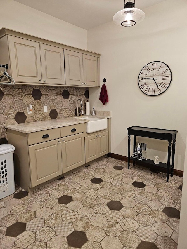 kitchen featuring a sink, baseboards, backsplash, and light countertops