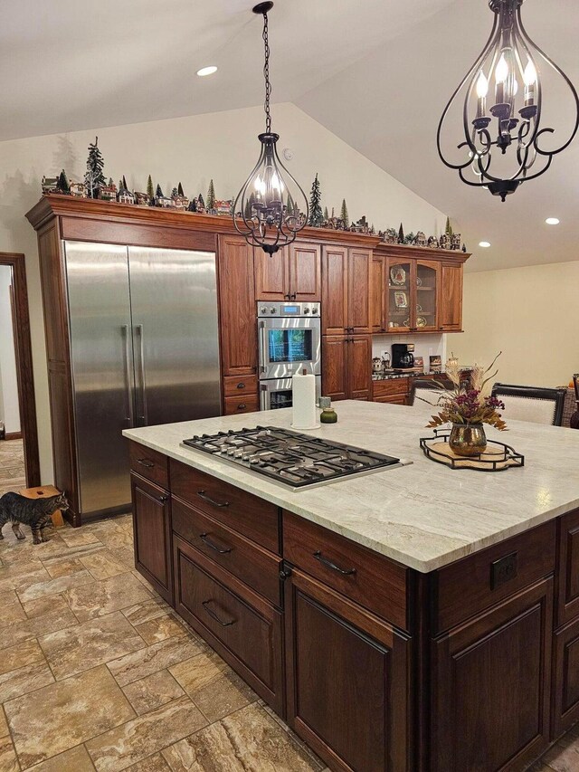 kitchen featuring pendant lighting, light stone counters, stainless steel appliances, glass insert cabinets, and vaulted ceiling