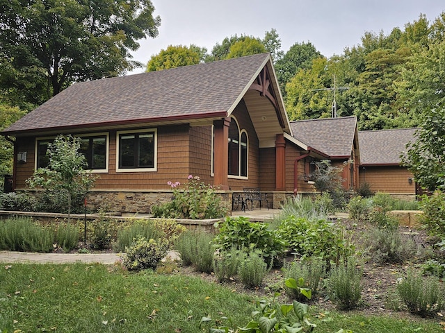 rustic home featuring stone siding, roof with shingles, and a patio