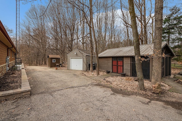 exterior space with metal roof, driveway, an outbuilding, and a detached garage
