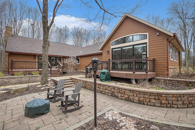 back of property featuring roof with shingles, a wooden deck, a patio, and a chimney