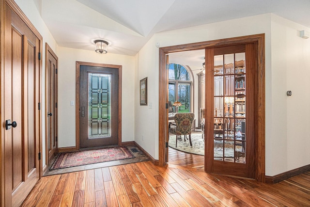 foyer entrance featuring baseboards, vaulted ceiling, and light wood-style floors