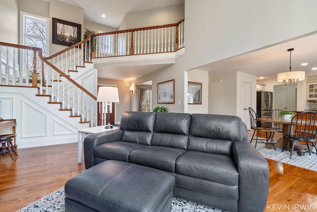 living area with wood finished floors, a high ceiling, recessed lighting, stairs, and a chandelier