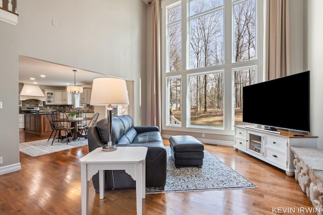 living area with an inviting chandelier, baseboards, light wood-type flooring, and a towering ceiling